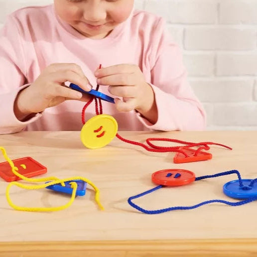 Child holding button like shapes and threading them on a red string.