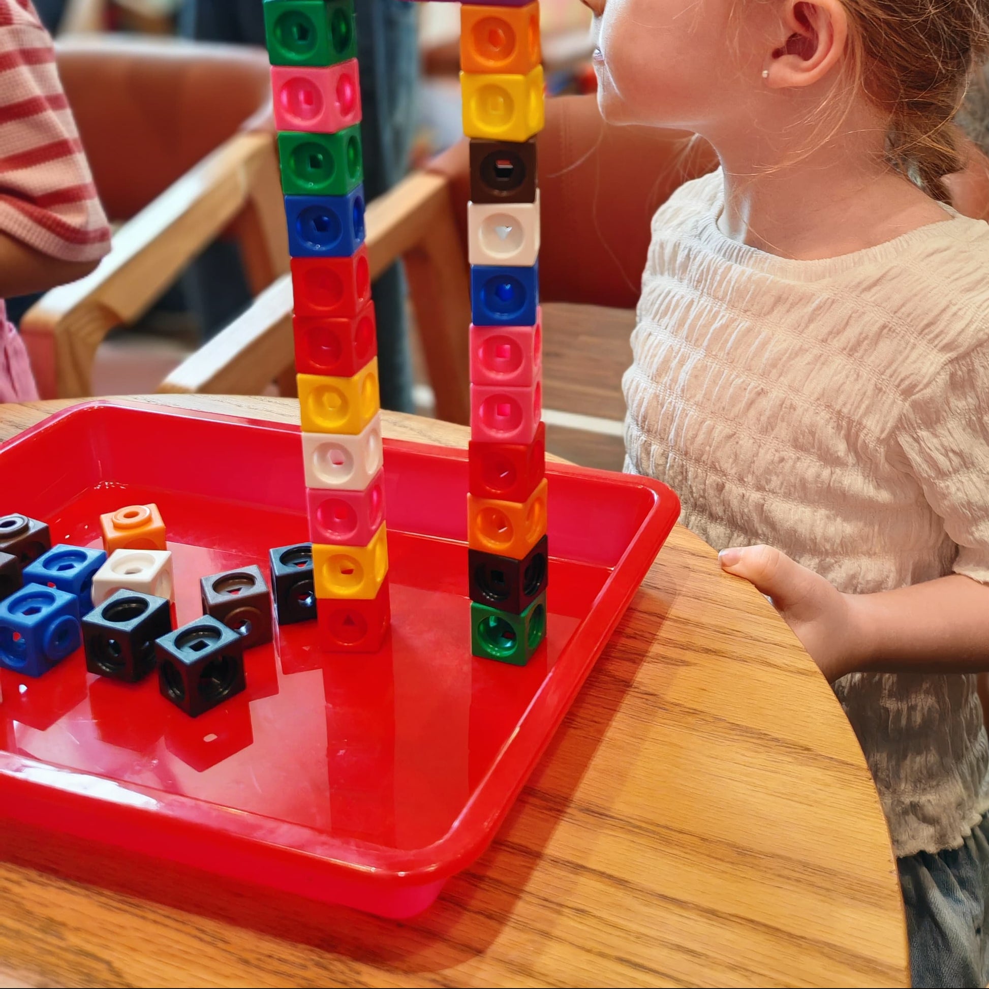 Child playing with colorful building blocks at a table, with people in the background.