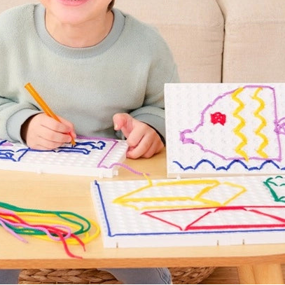 Child sitting at a table with our PathPad and strings, smiling.